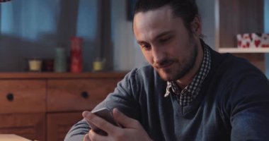 Akıllı telefonuna derinden odaklanmış bir adam, sıcak ve davetkar bir alanda modern iletişimi temsil ediyor.