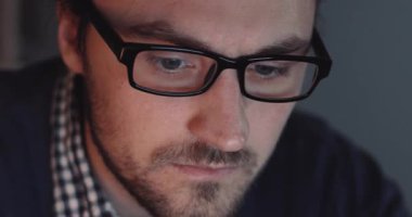 Gözlük takan odaklanmış bir birey, modern çalışma dinamiklerini temsil eden birden fazla dijital cihazla derinden ilgilenir.