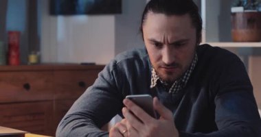 Bir adam telefonunu güzel tasarlanmış ve şık bir ofis ortamında kontrol ederken gözle görülür şekilde hayal kırıklığına uğramış görünüyor.