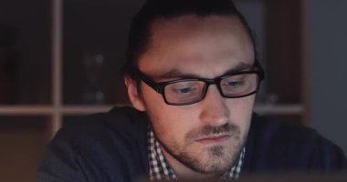 Kendini işine adamış ve odaklanmış bir profesyonel, loş bir alanda dizüstü bilgisayar üzerinde çalışırken derin düşüncelere dalmış.