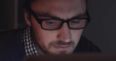 İşine dalmış, loş bir odada dizüstü bilgisayar kullanan, dikkate değer bir odaklanma ve kendini adamışlık gösteren bir adam.