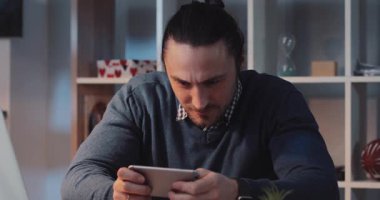 Çok odaklanmış ve tabletine dalmış bir adam şık ve çağdaş bir ofis yerinde oturuyor.