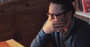 Düşünceli bir adam ahşap masasında yıpranmış bir defter üzerinde çalışıyor, sıcak çalışma alanına dalmış, fikirlerle dolu.