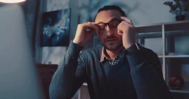 Odaklanmış bir adam, loş, modern ve şık bir çalışma alanında otururken dizüstü bilgisayarına derinden konsantre olur.