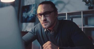 Bir adam yoğun bir şekilde dizüstü bilgisayarına odaklanmış, şık ve loş bir ofis atmosferinde çalışmaya dalmış.