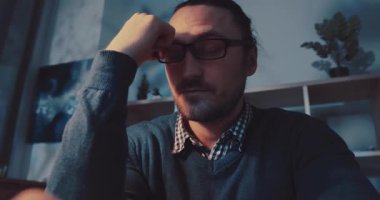 Gözlük takan bir adam, ofis masasındaki bir görevi rahat bir ortamda tamamlamaya yoğun bir şekilde odaklanır.