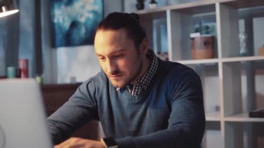 Bir adam masasında profesyonel bir işte çalışıyor. İyi aydınlatılmış, modern bir ofis alanında dizüstü bilgisayar kullanıyor.