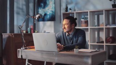 Modern bir ofiste dizüstü bilgisayarına odaklanmış, üretkenliğini ve yaratıcılığını sergileyen bir adam.