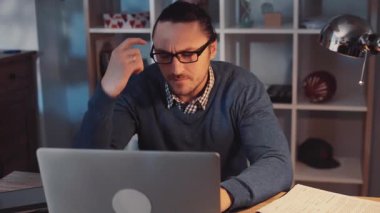 Ciddi ve kendini işine adamış bir birey, huzurlu bir çalışma ortamında dizüstü bilgisayarında çeşitli görevlerle derinden ilgilenir.