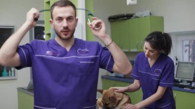 Veteriner bey, gülümseyen arka plan asistanına bakın veteriner kliniğindeki sevimli köpeği teftiş ediyor. Doktor.