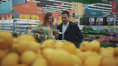 Portre genç çift sağlıklı ürünler üretiyorlar. Süpermarkette kız kıza alışveriş yapan meyve adam endüstrisinde konuşuyorlar. İnsanlar yetişkin pazarından keyif alıyorlar.