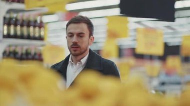 Markette elinde alışveriş arabasıyla yürüyen ciddi bir genç. Telefon ışığında alışveriş listesine bakıyor. Meyve alıcısı, yiyecek dükkânı, yetişkin, perakende satış mağazası, yavaş çekim.