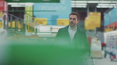 Markette elinde alışveriş arabasıyla yürüyen bir adam telefon ışığında alışveriş listesine bakıyor. Meyve alıcısı seçiyor. İş yemekleri, markete bakıyor.