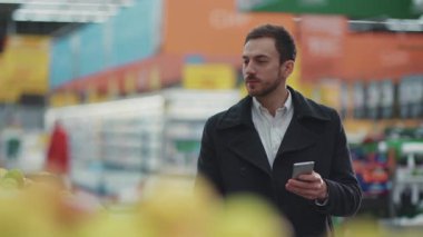 Yüzünüzü kapatın. Süpermarkette alışveriş arabasıyla yürüyen genç adam. Müşterilerin alışveriş listelerine bakıyor.