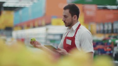 Satıcı, süpermarkette sebze işinde tablet bilgisayar kullanır. Güzel, taze ürünler, perakende satış yapan, genç, sağlıklı alışveriş merkezi modeli alışveriş ürünlerini seçen...