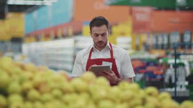 Portre satıcısı, süpermarkette sebze işinde tablet bilgisayar kullanıyor. Güzel, taze ürünler, perakende satış yapan, genç, sağlıklı alışveriş merkezi modelli alışveriş ürünlerini seçiyor.