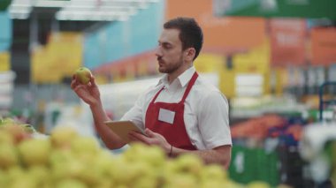 Gülümseyen satıcı, süpermarkette sebze işinde tablet bilgisayar kullanıyor. Güzel, taze ürünler, perakende satış yapan, genç, sağlıklı alışveriş merkezi ürünleri seçiyor. Küçük işler yapıyor.