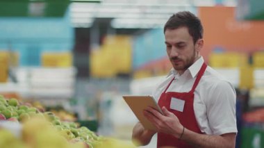 Genç satıcı, süpermarkette tablet bilgisayar kullanıyor. Kamera, sebze, güzel, taze ürün, perakende, yiyecek, alışveriş merkezi, küçük, sağlıklı alışveriş merkezi ürünleri seçiyor.