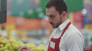 Süpermarkette mutlu yüz satan adam bak, gülümse, sebze, sebze, taze ürün, perakende işçisi, yiyecek, alışveriş merkezinin sağlıklı genç portresini seç.