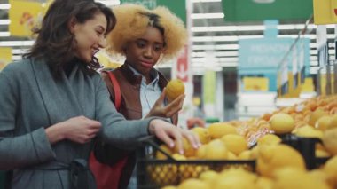 NEW YORK - 5 Nisan 2017: Süpermarkette limonu seçen iki güzel genç kadın gülümseyerek yiyecek alışverişi yapıyor, meyve alışverişi yapan siyah tüketici ailesi yeni market müşterilerini yavaş çekimde satın alıyor.