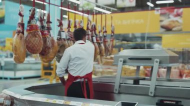 Yakın plan. Süpermarketteki et reyonunda satıcı dans ediyor. Market marketi, sebze pazarı, küçük dansçı, erkek, güzel gülümseme işçisi, yiyecek.