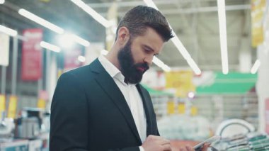 Genç sakallı adam, teknoloji mağazası el işi elektronik el alışverişi, internet teknolojisi, yavaş çekim portresi yakışıklı çekici bir şekilde yakın çekimde satış danışmanıyla konuşmak için 