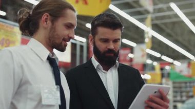 Genç sakallı adamla yakışıklı bir satıcı konuşması. Teknoloji mağazasında dokunmatik tablet bilgisayar kullanıyor. Elektronik el alışverişi, internet alışveriş merkezi yavaş çekim portresi.