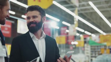 Genç sakallı adamla gülümseyen satıcı sohbeti teknoloji mağazasında cep telefonu kullanıyor. Elektronik el alışverişi, internet alışveriş merkezi yavaş çekim portresi. Yakışıklı, çekici bir portre.