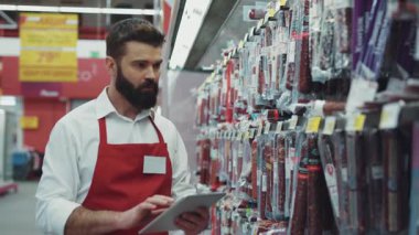 NEW YORK - 5 Nisan 2017: Et bölümündeki süpermarkette sakallı ciddi bir satıcı tablet bilgisayar kullanıyor.