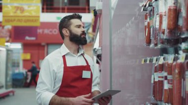 Kapatın sakallı satıcı marketteki süpermarkette tablet bilgisayar kullansın. Mutlu iş dünyası. Perakende satış işçisi gıdaları.