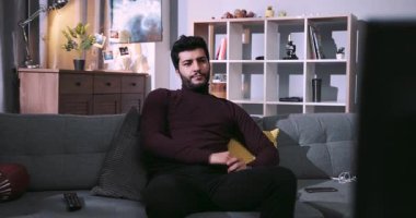 NEW YORK - 5 Nisan 2017: Yakışıklı, vahşi bir adam kanepede oturur, en sevdiği kanalı açar, görünenden hayal kırıklığına uğrar, başka bir televizyon programına geçer, vazgeçer, gider. Kanepe patatesi, tembel gün, ev eğlencesi. Erkek portresi