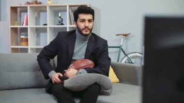 Şık kıyafetli sakallı adam yastığı tutuyor ve Amerikan futbol topu, maçı izlerken en sevdiği takım için tezahürat yapıyor. Kazanan, amigo, eğlenen. Yavaş çekim, kamera dengeleyici çekim