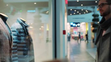 Mağazanın vitrinine erkek kıyafetleriyle bakan genç ve çekici bir adam. Yılbaşı için özel tasarım, Noel ağacı mağazası, alışveriş mağazası, yavaş çekim mağazası.