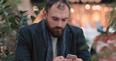 Genç çekici bir adam alışveriş merkezinde oturup gülümsüyor portreyi yakından çekiyor mutlu bir akıllı telefon yakışıklı yeni yıl alışverişini bekliyor yeni yıl ışıkları internetin yavaş çekim ışıkları