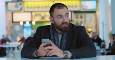 Yakışıklı genç adam telefon kullanıyor alışveriş merkezinde gülümsüyor yakın portrede mutlu oluyor kafeterya alışverişi bekliyor yeni yıl ışıkları akıllı mobil internet yavaş çekim