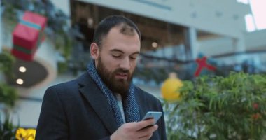 Portre genç çekici adam mutlu olmak için telefon başında duruyor. Yakından alışveriş yapıyor. Yılbaşı cep telefonu, akıllı telefon, günlük internet, yavaş çekim.