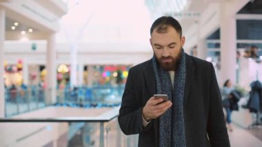 Çantalı genç ve çekici bir adam telefon yürüyüşü yapıyor. Kameraya gülümseyen bir alışveriş merkezine gidiyor. Mutlu bir portre, alışveriş bekliyor.