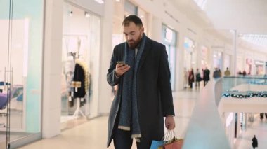 Çantalı çekici genç adam telefon kullanmayı bıraktı. Gülümsemeyi bıraktı. Mutlu portre yakışıklı, alışveriş bekliyor.