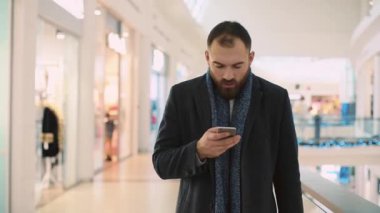 Çekici bir adam telefon yürümeyi bıraktı. Alışveriş merkezinde gülümsemeyi kesti. Mutlu portre yakışıklı, alışveriş bekliyor.