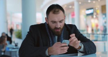 Yakışıklı genç adam telefon kullanıyor alışveriş merkezinde gülümsüyor yakın portre çekimde mutlu oluyor kafeterya alışverişi bekliyor yeni yıl ışıkları akıllı telefon mobil internet yavaş çekim