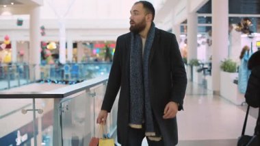 Ciddi, genç, çekici ve çantalı bir adam. Saate bak. Alışveriş merkezinde acele et.