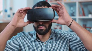 Genç ve çekici bir adam sanal gerçeklik gözlüğü kullanıyor. Kanepede oturmuş gülümsüyor. Oyun evini kapatıyorlar.