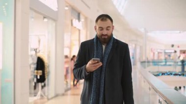 Çantalı genç çekici bir adam telefon yürüyüşü yapıyor. Alışveriş merkezinde gülümsemeyi kesiyor. Mutlu portre bekliyor.