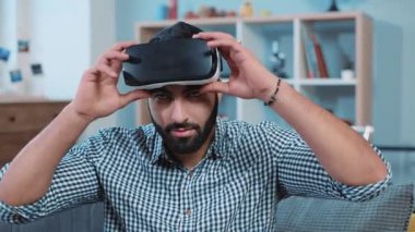 Yakışıklı genç adam sanal gerçeklik gözlüğü takıyor. Ev portresindeki koltukta oturmuş gülümseyen kameraya bakın. Tasarım oyunu 3D internet teknolojisi yeniliği.