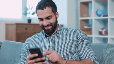 Çekici genç adam telefonda mesaj yazıyor gülümsüyor. Kanepede oturup ev portresi çekiyor. Akıllı telefonları kapatıyor, elektronik uygulama kullanıyor.