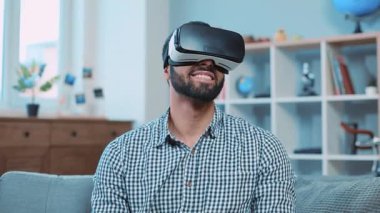 Gülümseyen çekici adam koltukta oturup sanal gerçeklik gözlüğü kullanıyor rahatlayın ev portresi kapatın internet teknolojisi yenilikleri yavaş çekim
