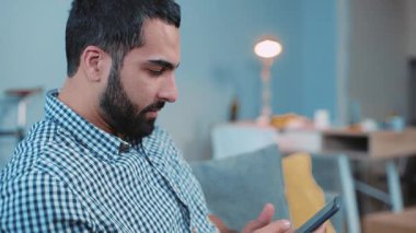 Yakışıklı genç adam telefonu kullan gülümse ve mutlu ol kanepeye otur ev portresi kapat akıllı telefon elleri elektronik uygulama mesajı yaz mutlu bağlantı eğlence yaşam tarzı iletişimi dokun