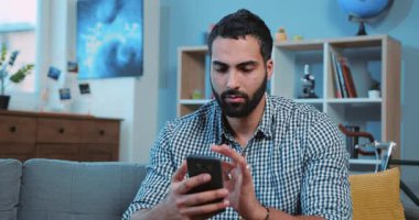 Kapat çekici genç adam telefonda yazarken gülümse kanepeye otur ev portresi akıllı telefon elektronik uygulama bağlantı kurma yaşam tarzı iletişimi dokun