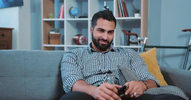 Genç, gülümseyen, bira içen, televizyon izleyen bir adamın portresi. Uzaktan kumandayı evde yalnız başına bir kanepede tutuyor. Şişeci çocuk kanepesi.