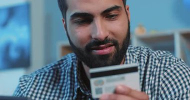 Çevrimiçi satın alan çekici genç adam, telefon ve kredi kartını kanepenin üzerinde kullanıyor. Cep telefonu, telefon, cep telefonu, telefon, el, hayat tarzı, akıllı internet teknolojisi bankası, nakit para tutuyor.